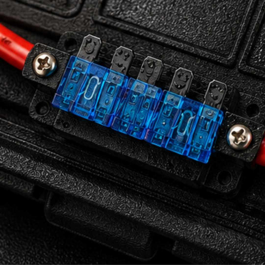 Close-up of a fuse holder with blue fuses and red and black wires on a black background.