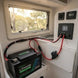 Lithium battery connected to a power panel inside a vehicle with a window showing trees outside.