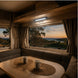 Interior of a camper van with a table and two mugs, overlooking a scenic view at sunset.