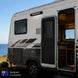 Small trailer with open door, designed in Australia, near a body of water.