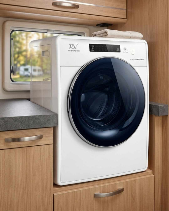 White RV washer dryer in a caravan with wooden cabinets and a window.