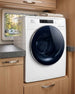 White RV washer dryer in a caravan with wooden cabinets and a window.
