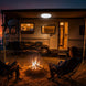Two people sitting by a campfire in front of a vintage-style RV at night.