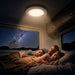 Family lying in bed under a night sky view with a light fixture above.