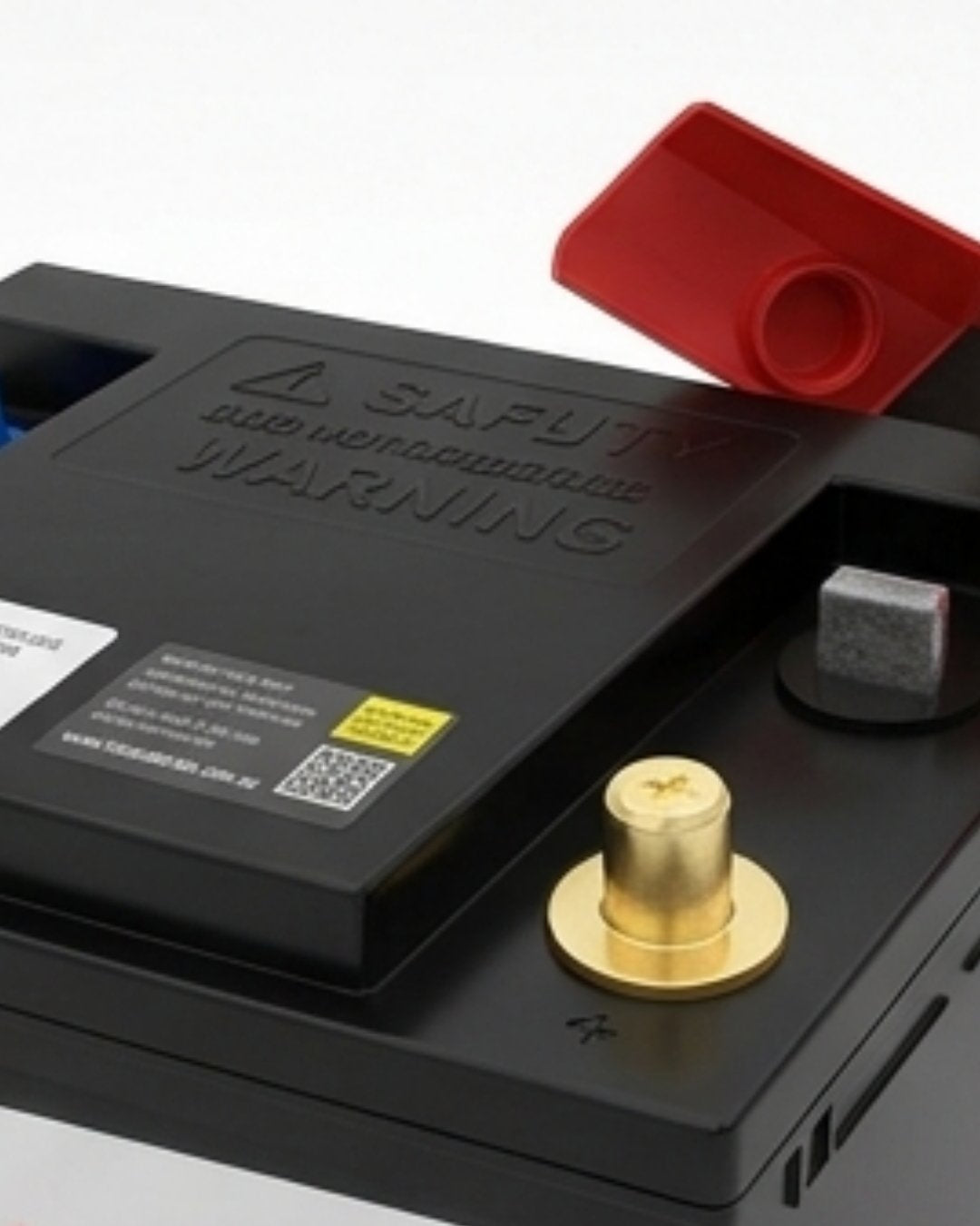 Close-up of a car battery with visible warning label and red positive terminal cover.