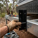 Hand with tool holding metal bracket against a truck bed outdoors