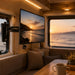 Interior of a vehicle with a TV displaying a sunset over water, a couch, and a coffee cup on a table.